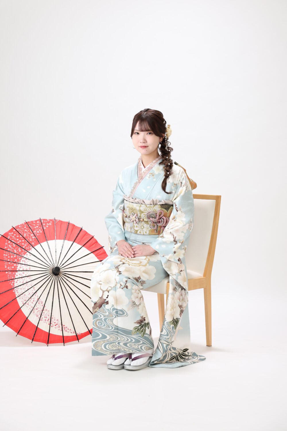 白背景で椅子に腰かける水色の振袖を着た女性