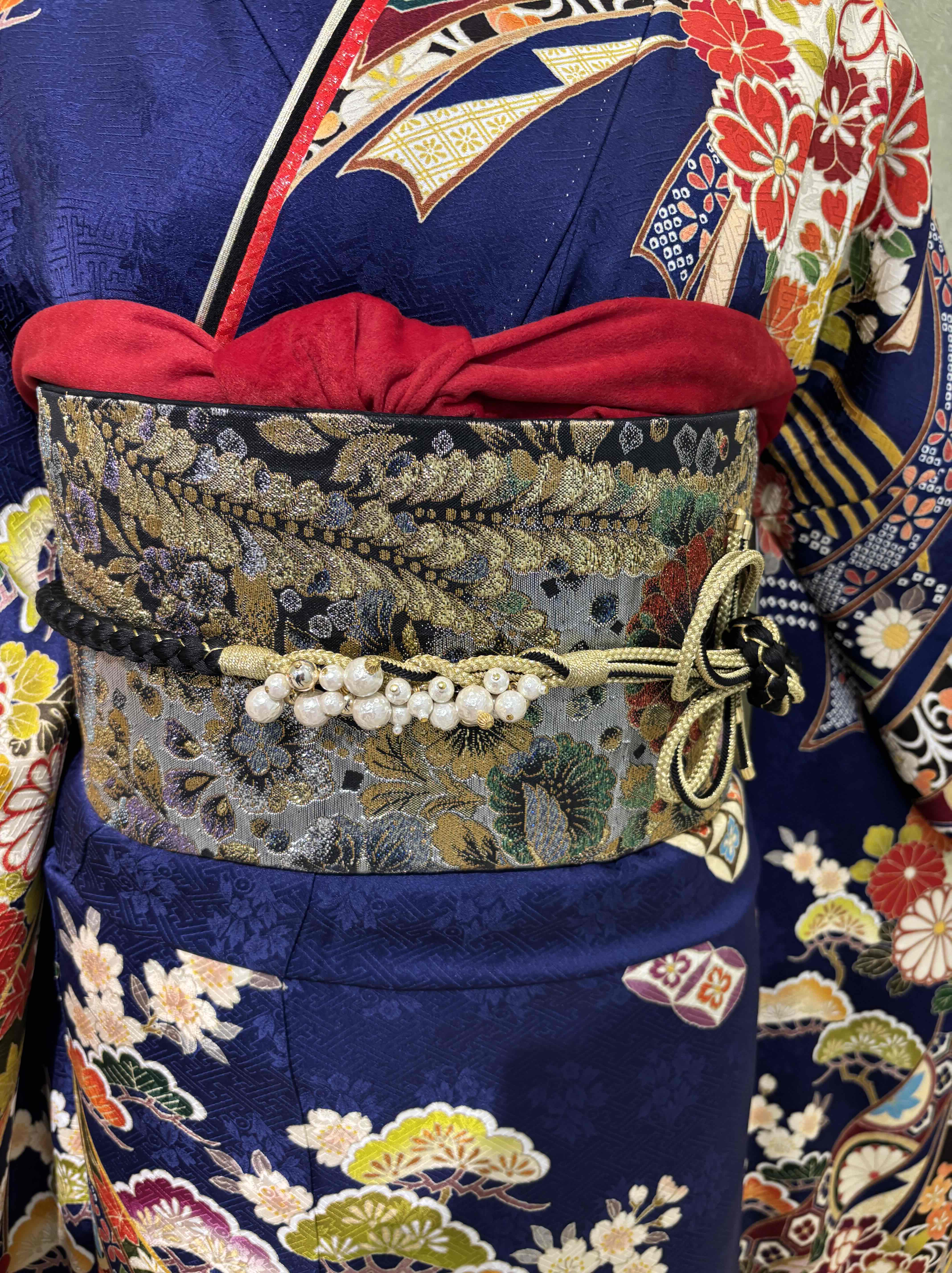 黒地に金彩が映える重厚感のある帯に赤のベロア素材の帯揚げや飾りの大きい帯締めで今どき感をプラス