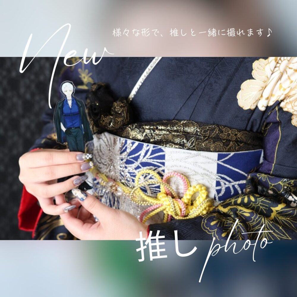 振袖姿での推し活フォト。紺色の振袖を着たお客様の手元アップ。帯の前で男性キャラクターのアクリルスタンドを持っている。画像内テキスト：『様々な形で、推しと一緒に撮れます♪』『New 推し photo』
