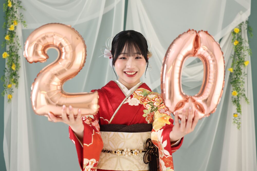 20のバルーンを持って成人式の振袖前撮りをする赤い振袖のお嬢様