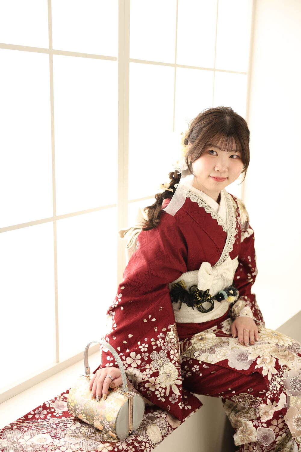 窓辺に座っている赤い振袖をきたお嬢様の前撮り写真