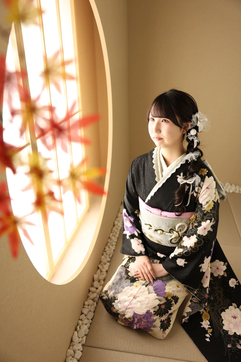 黒地の振袖で丸窓のそばに座ったお嬢様